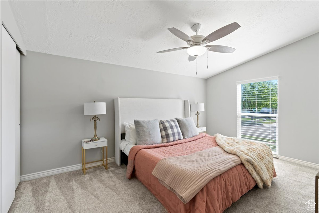 Bedroom featuring baseboards, light carpet, a textured ceiling, ceiling fan, and vaulted ceiling