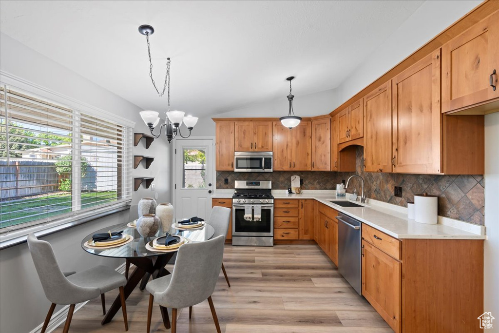 Kitchen with stainless steel appliances, a sink, light countertops, light wood-style floors, and decorative backsplash