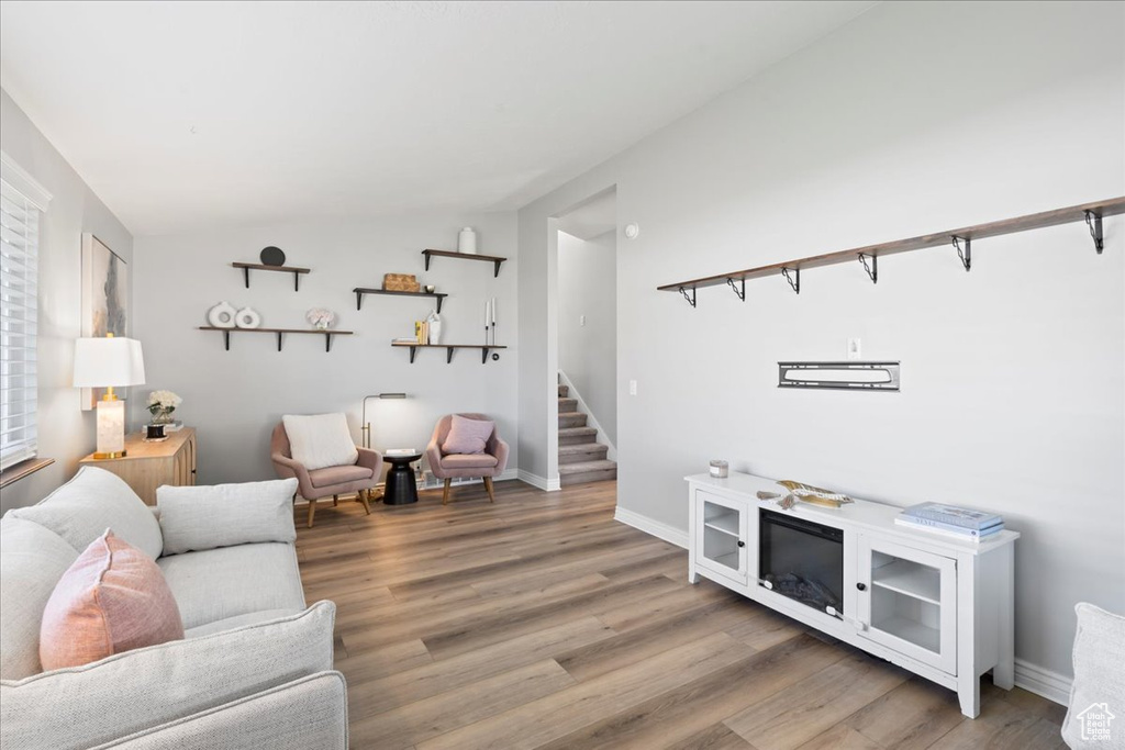 Living room with stairway, vaulted ceiling, light wood finished floors, and baseboards
