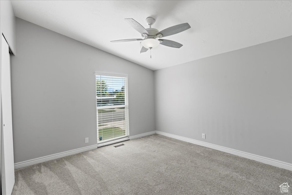 Carpeted spare room featuring ceiling fan, lofted ceiling, and baseboards