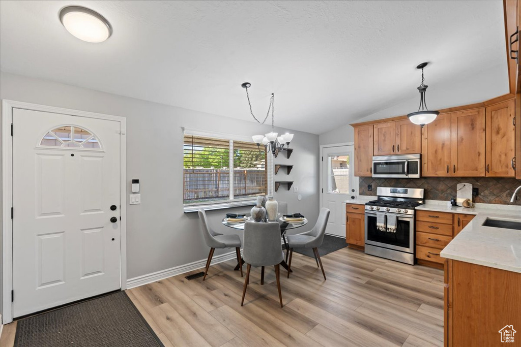 Kitchen with appliances with stainless steel finishes, a sink, light wood finished floors, tasteful backsplash, and lofted ceiling