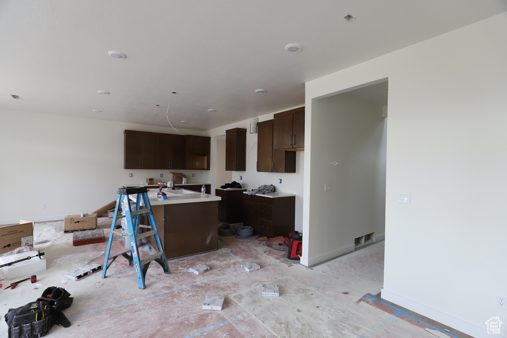 Kitchen with dark brown cabinetry, a center island with sink, light countertops, and baseboards