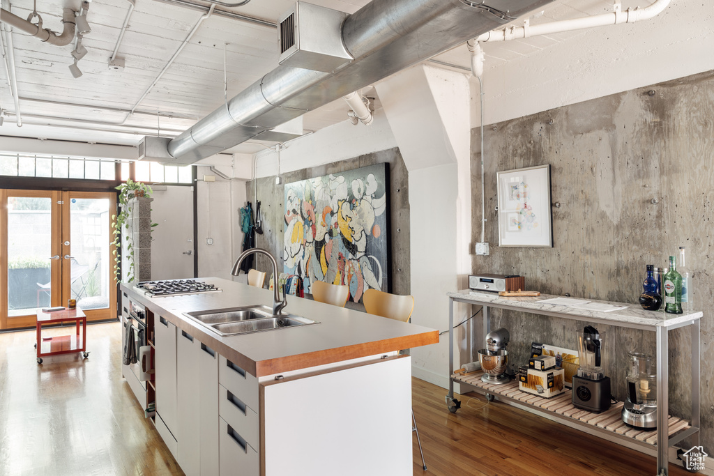 Kitchen featuring light wood finished floors, stainless steel gas cooktop, a kitchen island with sink, white cabinetry, and light countertops