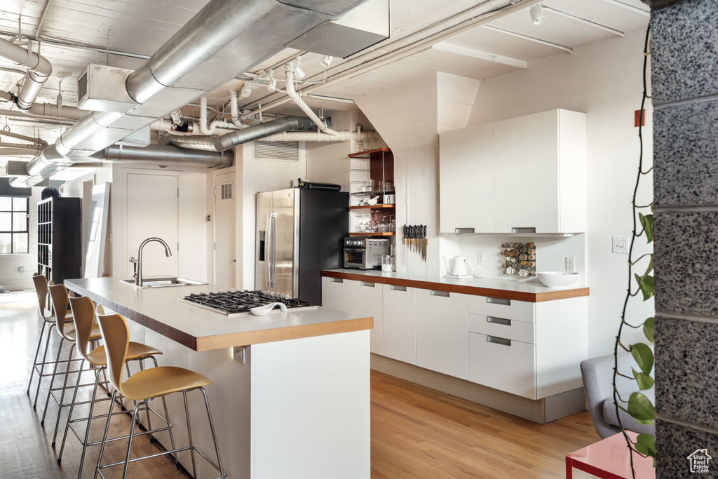 Kitchen with a sink, a breakfast bar area, white cabinetry, modern cabinets, and appliances with stainless steel finishes
