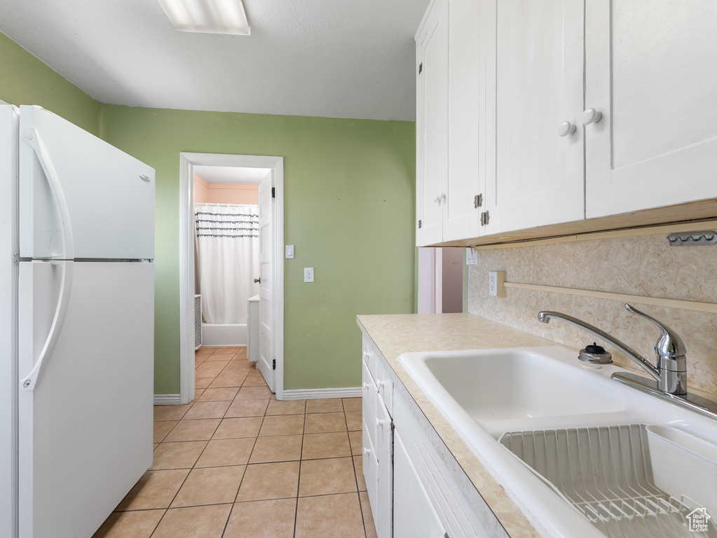 Kitchen featuring freestanding refrigerator, a sink, white cabinets, light tile patterned floors, and light countertops