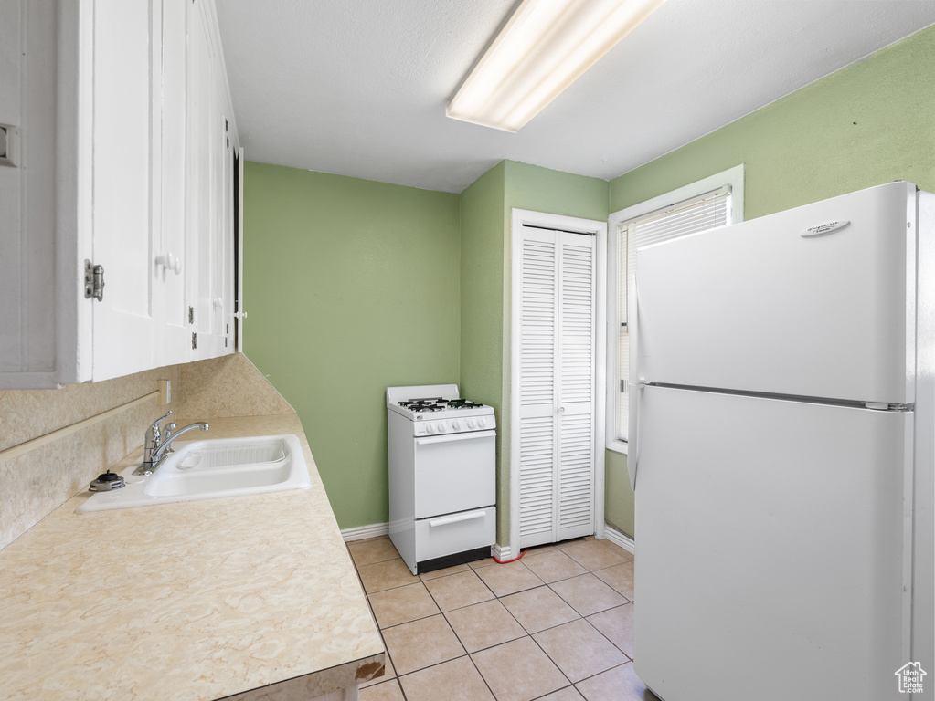Kitchen with white appliances, a sink, light countertops, light tile patterned flooring, and baseboards