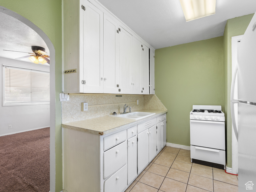 Kitchen featuring white appliances, a sink, arched walkways, white cabinetry, and light countertops