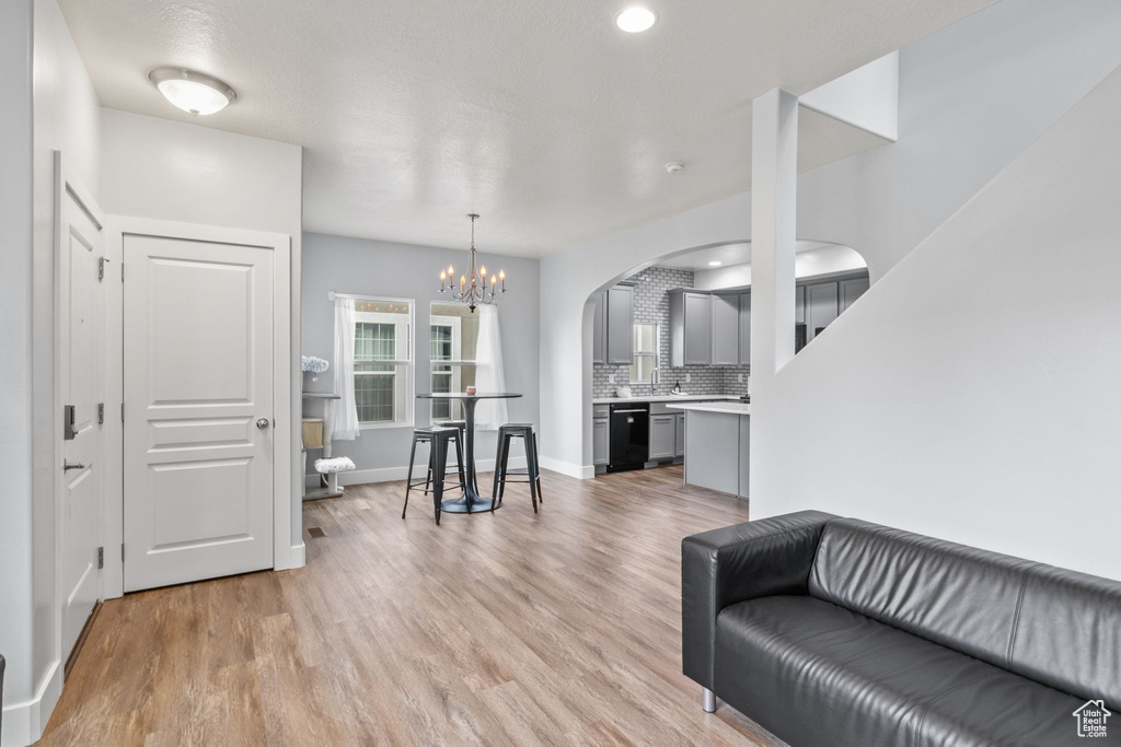 Living room featuring arched walkways, light wood finished floors, a chandelier, baseboards, and recessed lighting