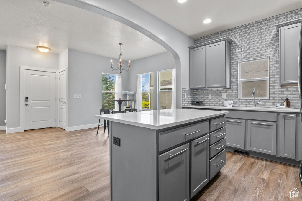 Kitchen with gray cabinetry, a chandelier, arched walkways, light countertops, and light wood-style floors