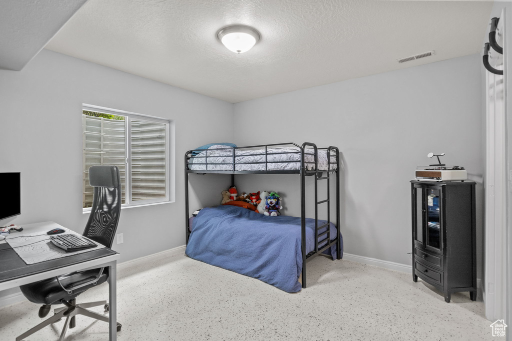 Bedroom with a textured ceiling, speckle patterned floor, a desk, and baseboards