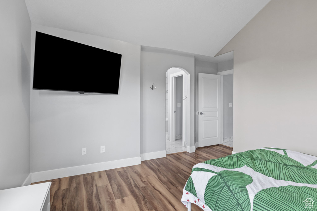 Bedroom featuring arched walkways, wood finished floors, baseboards, and vaulted ceiling