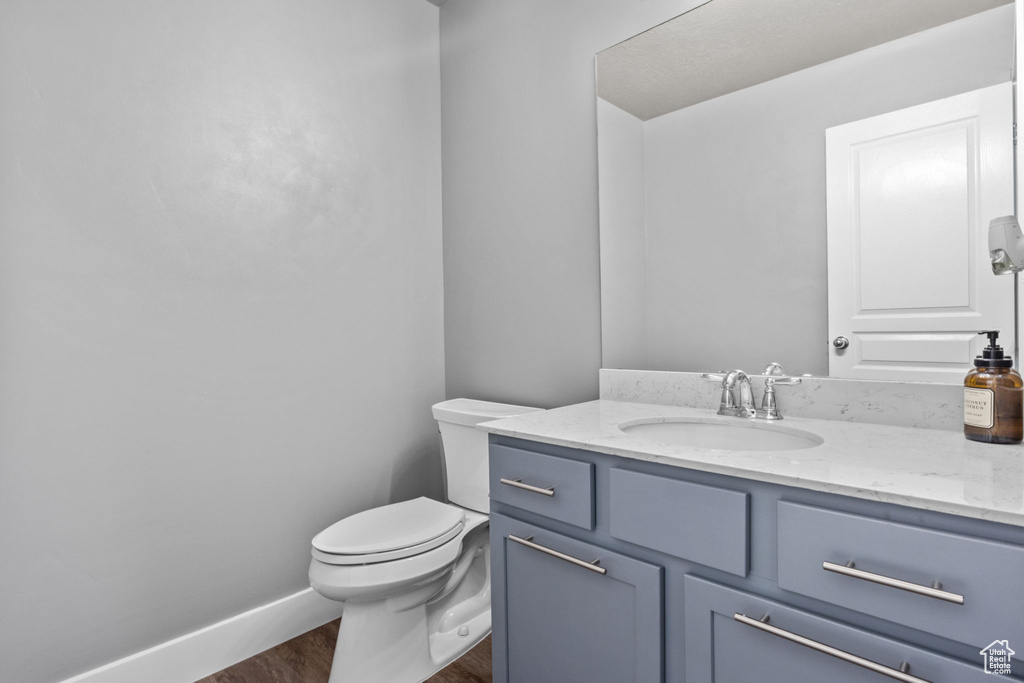 Half bathroom with wood finished floors, toilet, and vanity
