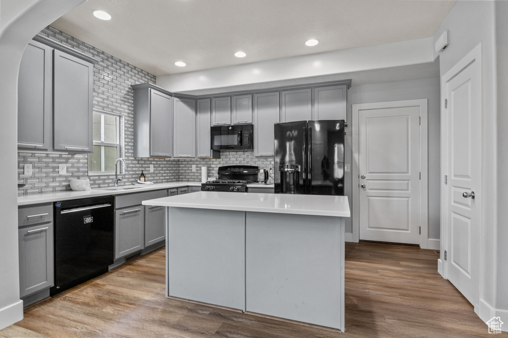 Kitchen with black appliances, gray cabinets, a sink, light countertops, and backsplash