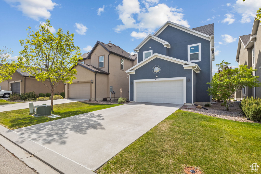 Traditional-style home featuring concrete driveway, a garage, a front lawn, and stucco siding