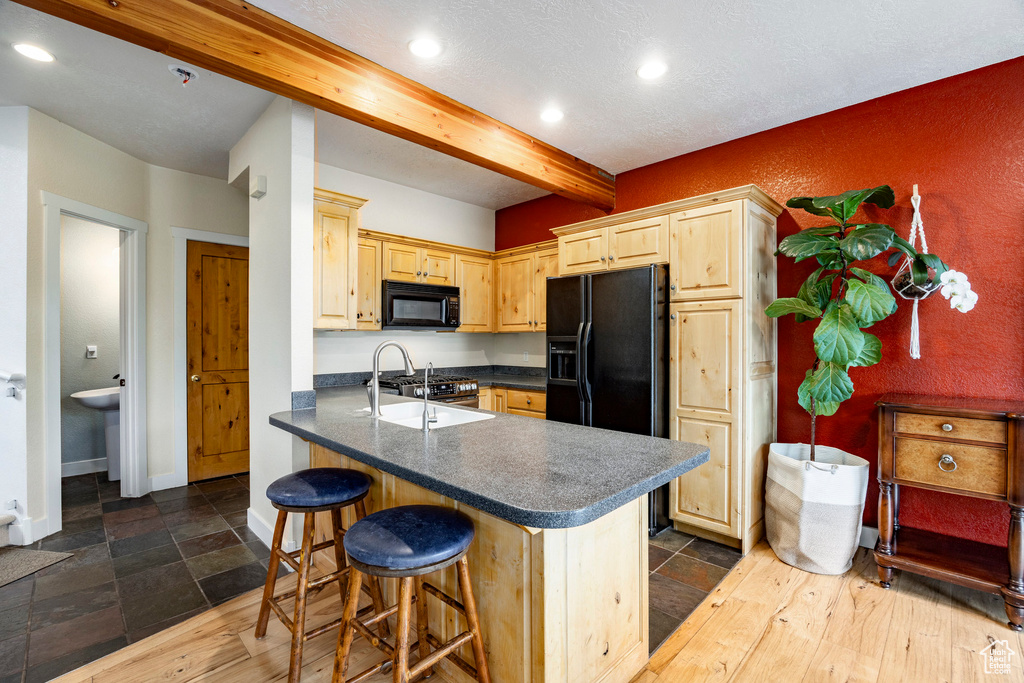 Kitchen with black appliances, a sink, beam ceiling, dark countertops, and light brown cabinetry