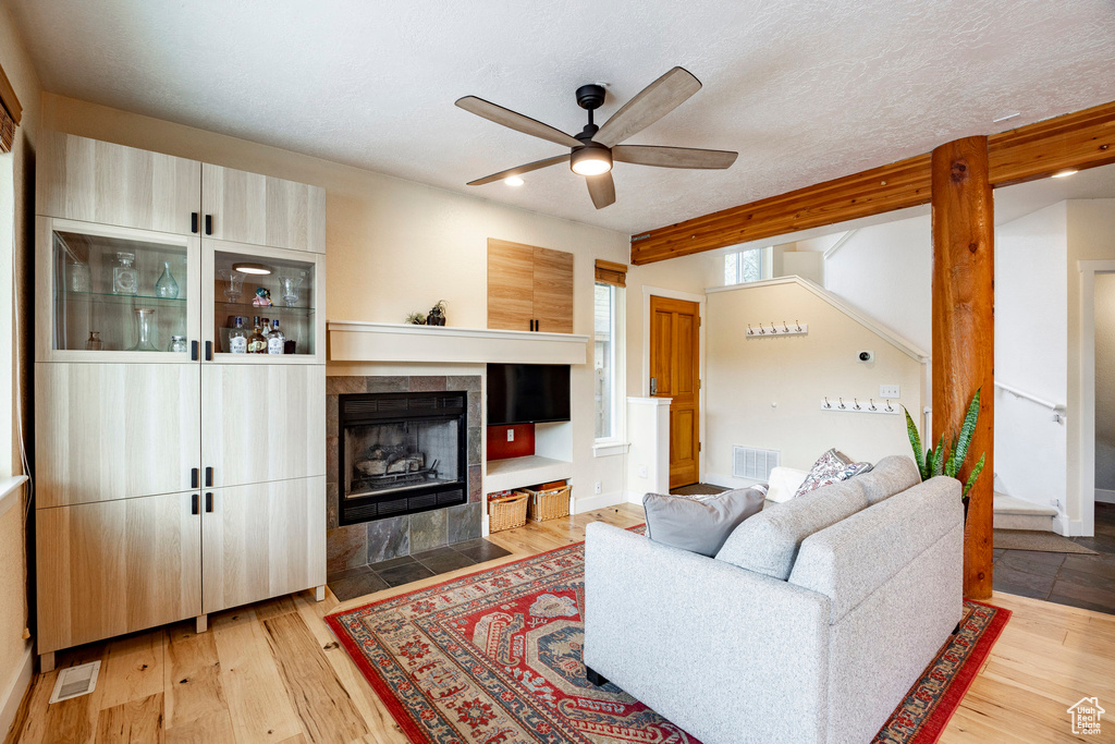 Living area featuring a ceiling fan, a fireplace, light wood finished floors, stairway, and beam ceiling