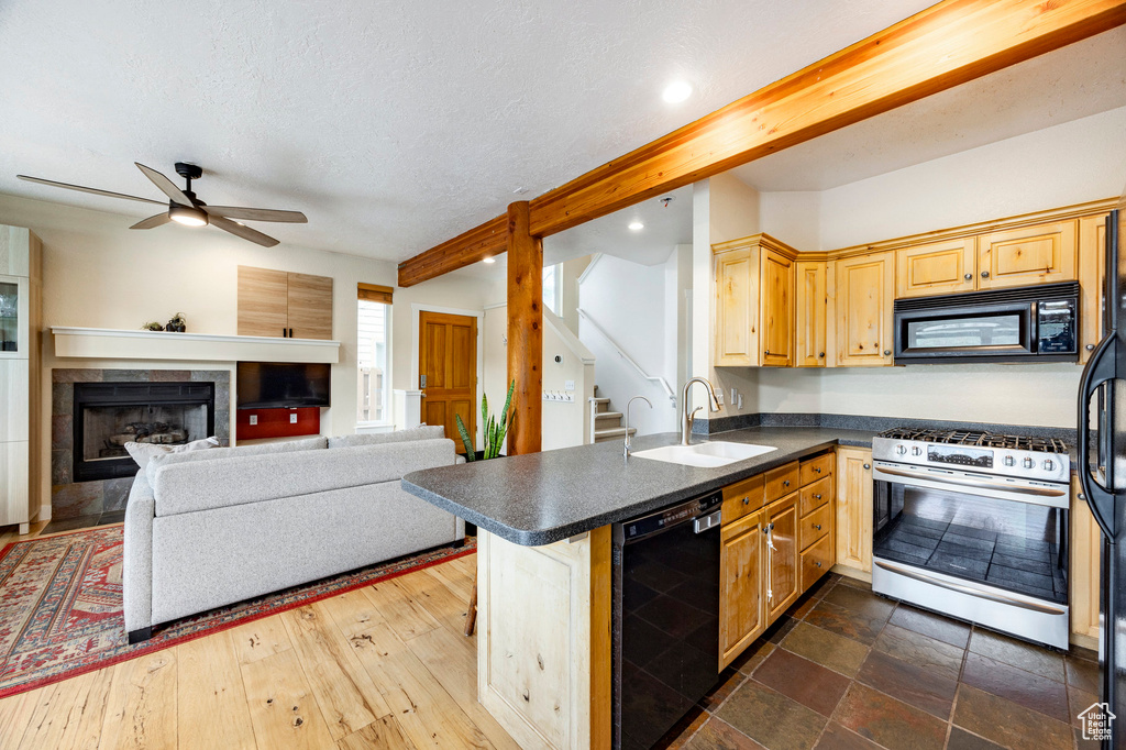 Kitchen featuring black appliances, a sink, dark countertops, beamed ceiling, and a ceiling fan
