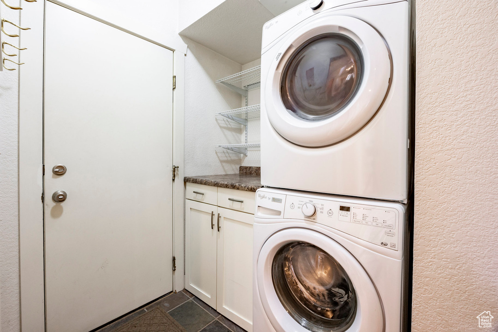 Washroom with estacked washer and dryer, cabinet space, and a textured wall