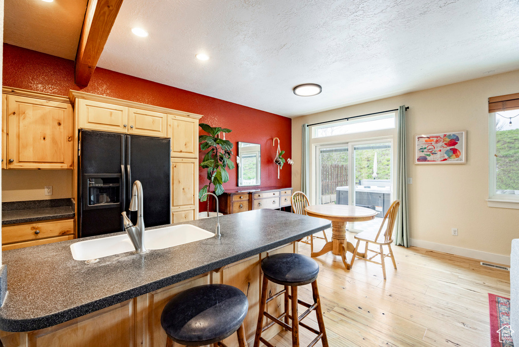 Kitchen featuring a sink, black fridge, a breakfast bar area, light brown cabinetry, and baseboards