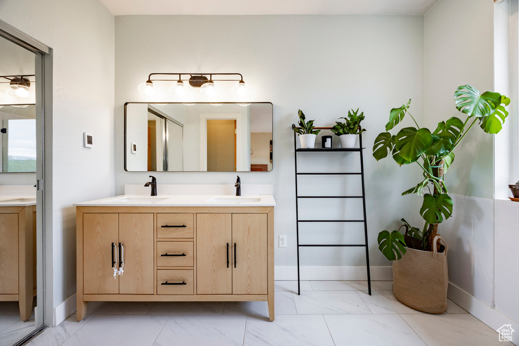 Bathroom featuring marble finish floors, double vanity, and baseboards
