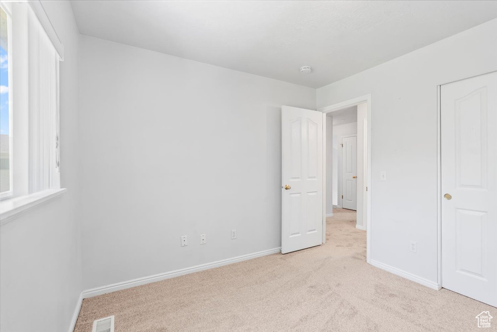 Unfurnished bedroom with light carpet and baseboards