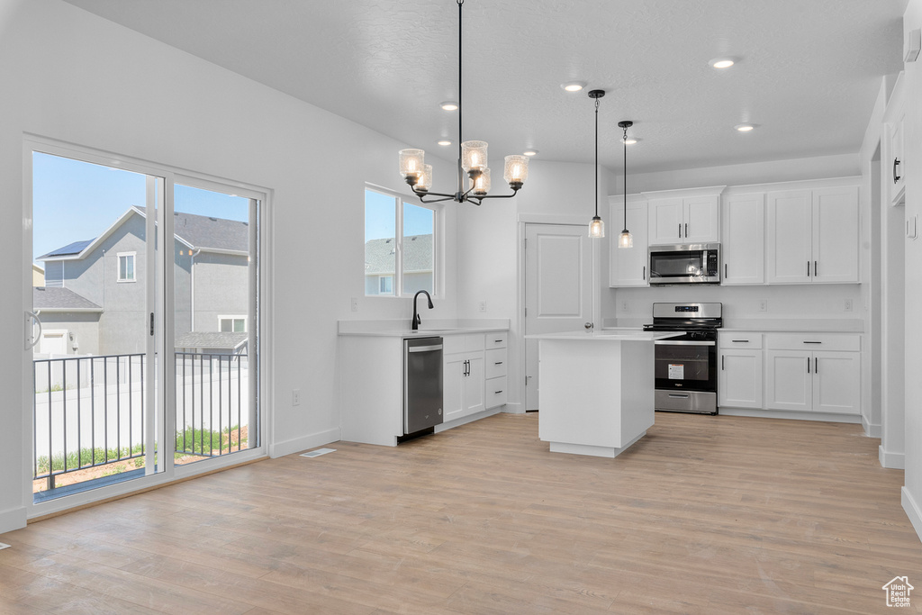 Kitchen featuring appliances with stainless steel finishes, a chandelier, light countertops, a center island, and light wood-style flooring