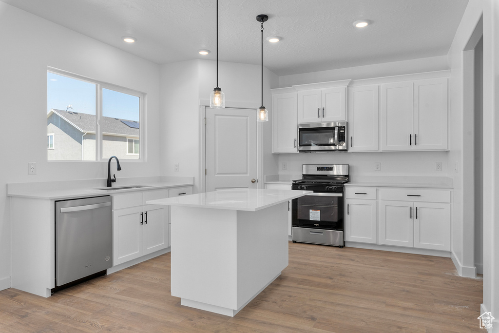 Kitchen featuring stainless steel appliances, a sink, white cabinets, light countertops, and a center island