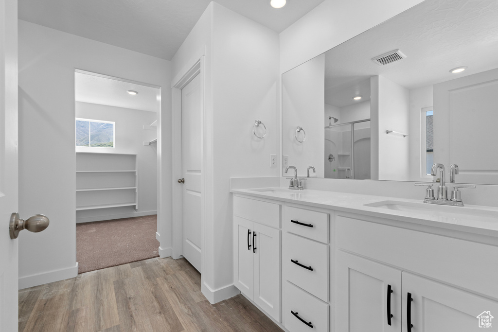 Bathroom featuring wood finished floors, a shower stall, double vanity, recessed lighting, and baseboards