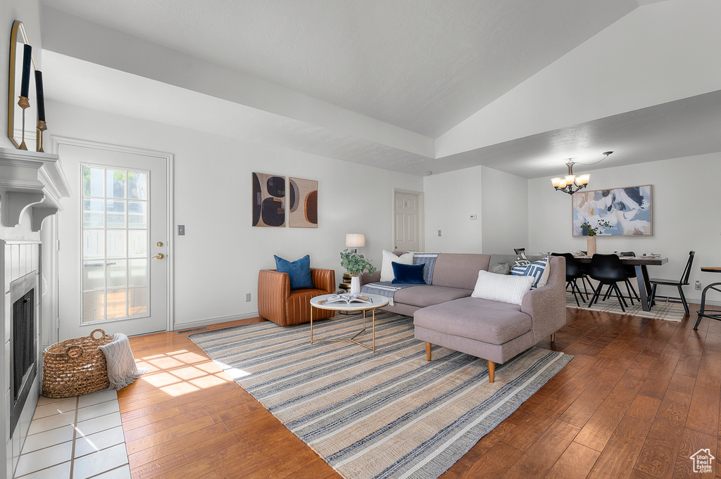 Living room featuring a chandelier, hardwood / wood-style floors, a fireplace, lofted ceiling, and baseboards
