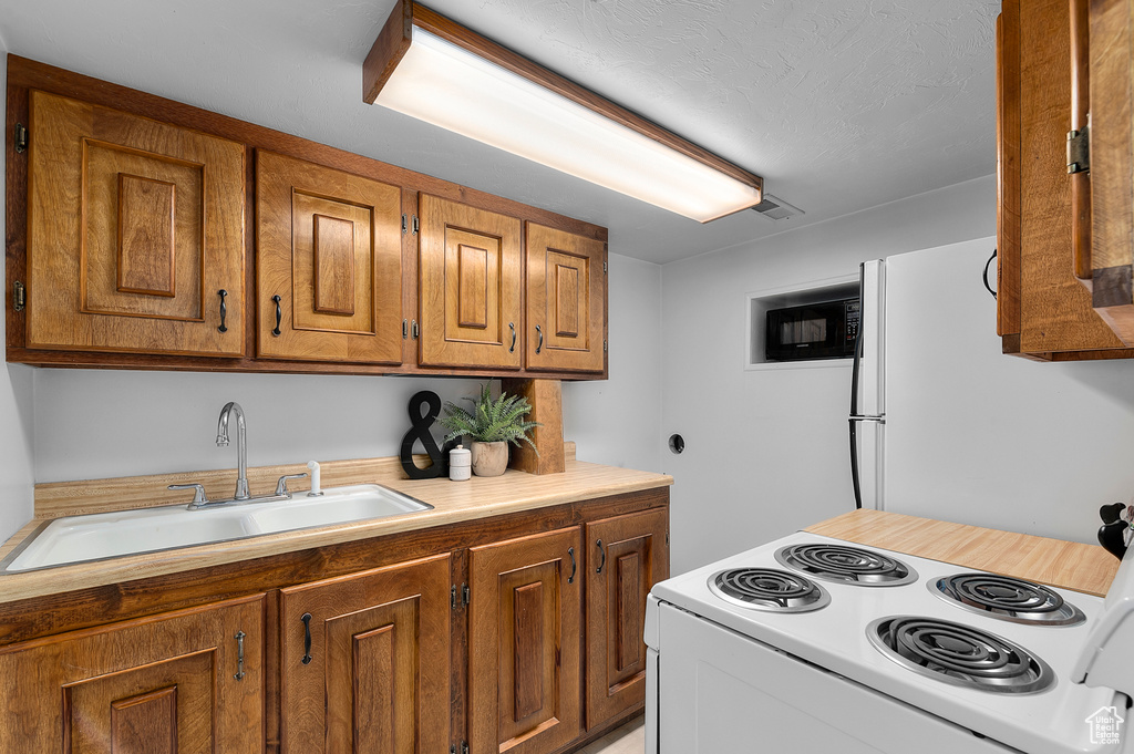 Kitchen with white appliances, a sink, and brown cabinetry