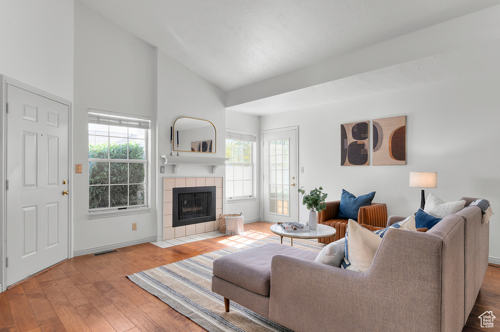 Living room featuring a tile fireplace, healthy amount of natural light, baseboards, wood finished floors, and a high ceiling