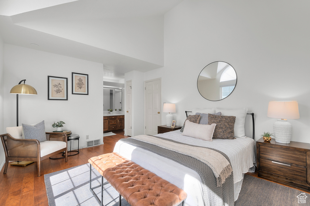 Bedroom with wood finished floors, high vaulted ceiling, connected bathroom, and baseboards