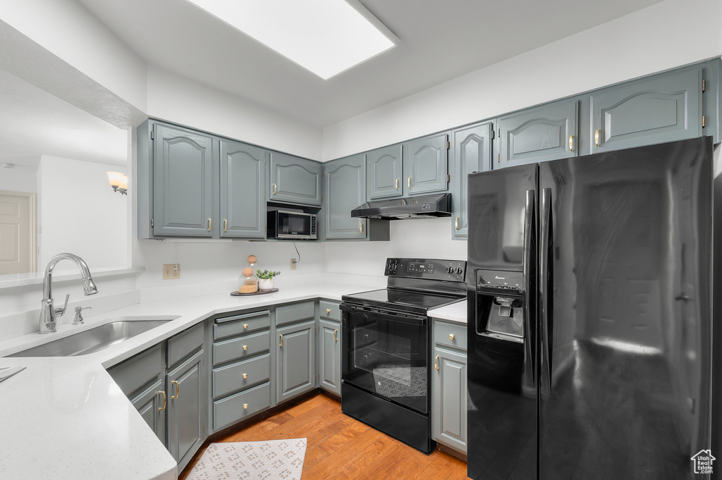 Kitchen featuring black appliances, a sink, under cabinet range hood, gray cabinets, and light wood-type flooring