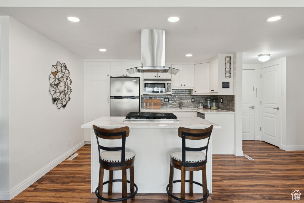 Kitchen featuring appliances with stainless steel finishes, exhaust hood, a kitchen breakfast bar, baseboards, and backsplash