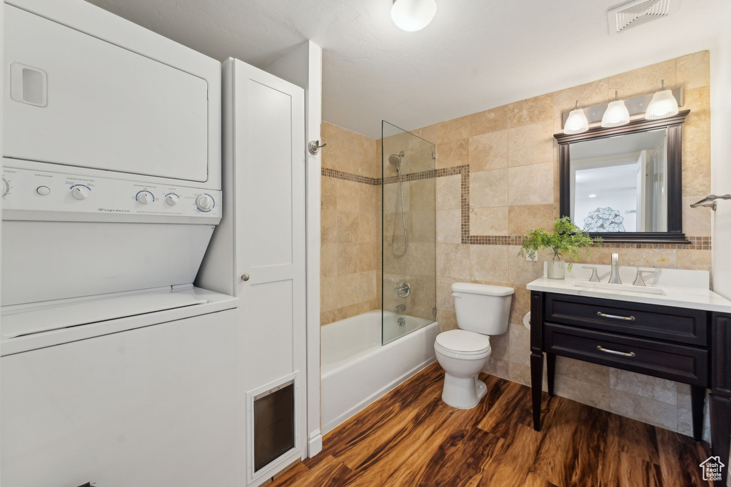 Full bathroom with estacked washer and dryer, wood finished floors, vanity, toilet, and tile walls