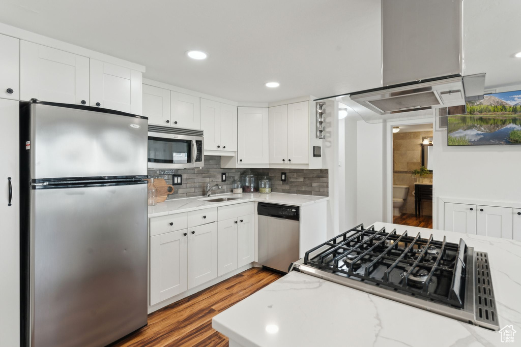 Kitchen with appliances with stainless steel finishes, white cabinetry, light wood finished floors, light stone countertops, and backsplash