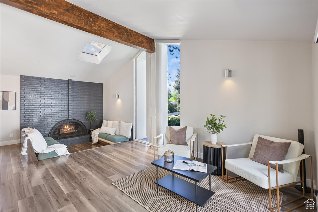 Living area featuring a skylight, wood finished floors, baseboards, and a brick fireplace