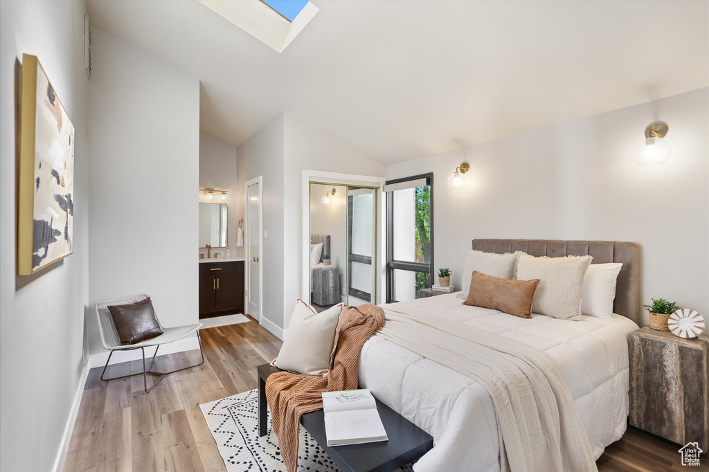 Bedroom featuring light wood finished floors, lofted ceiling, baseboards, a skylight, and ensuite bathroom