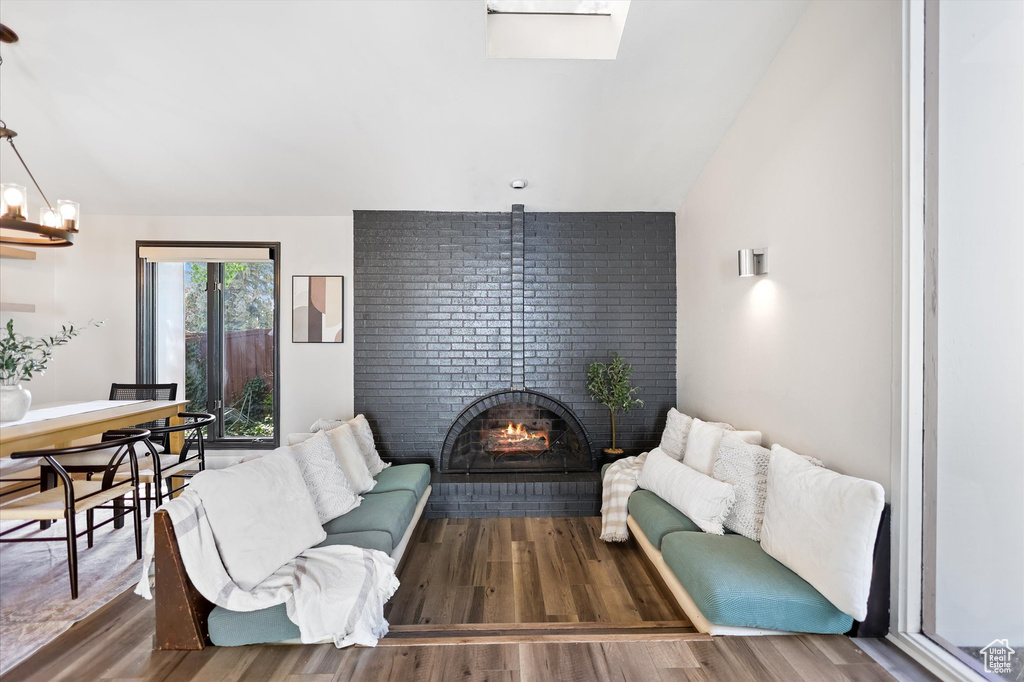 Living room featuring vaulted ceiling, a fireplace, wood finished floors, and a skylight