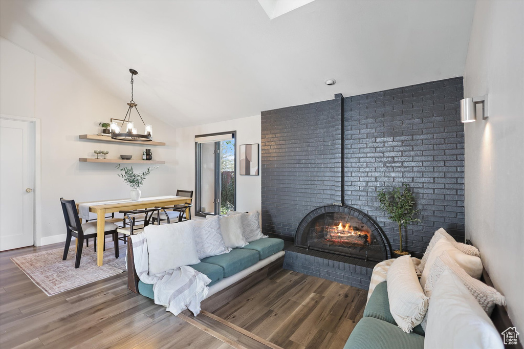 Living room featuring a chandelier, wood finished floors, vaulted ceiling, and brick wall