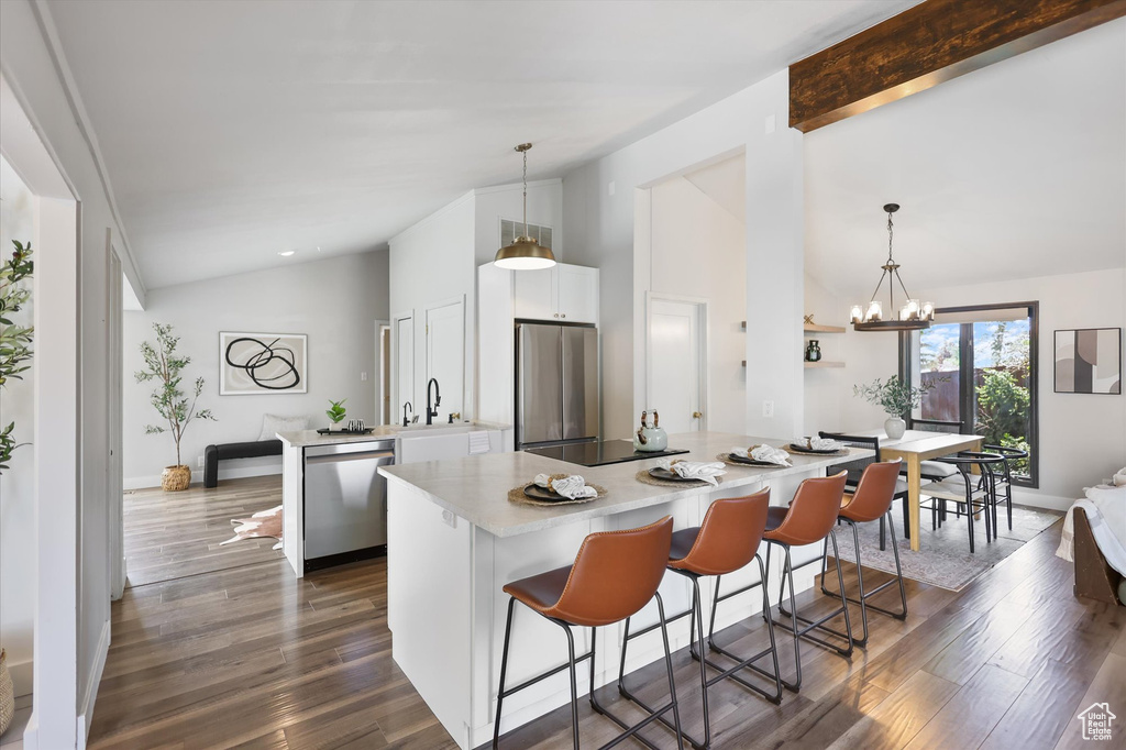 Kitchen with stainless steel appliances, a sink, white cabinets, light countertops, and a kitchen bar