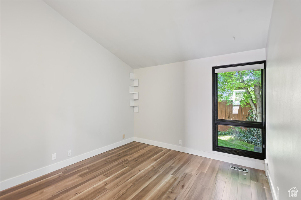 Unfurnished room featuring vaulted ceiling, wood finished floors, and baseboards