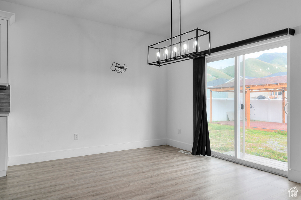 Unfurnished dining area featuring light wood-style flooring, a chandelier, and baseboards