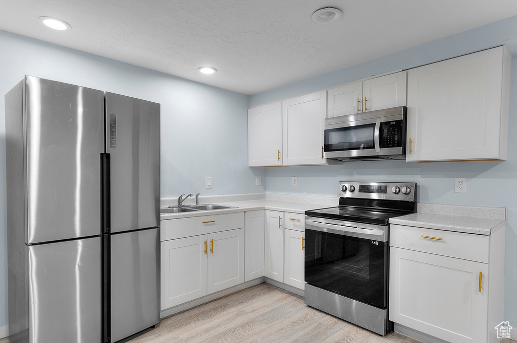 Kitchen featuring stainless steel appliances, a sink, light countertops, light wood-type flooring, and white cabinetry