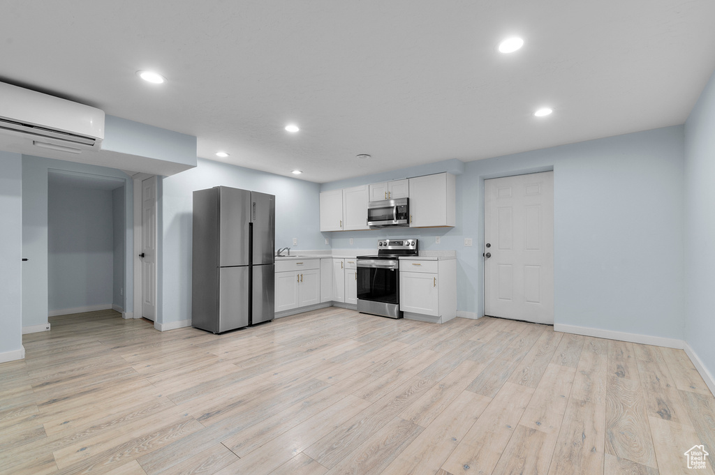 Kitchen with appliances with stainless steel finishes, a wall mounted AC, light countertops, baseboards, and white cabinets