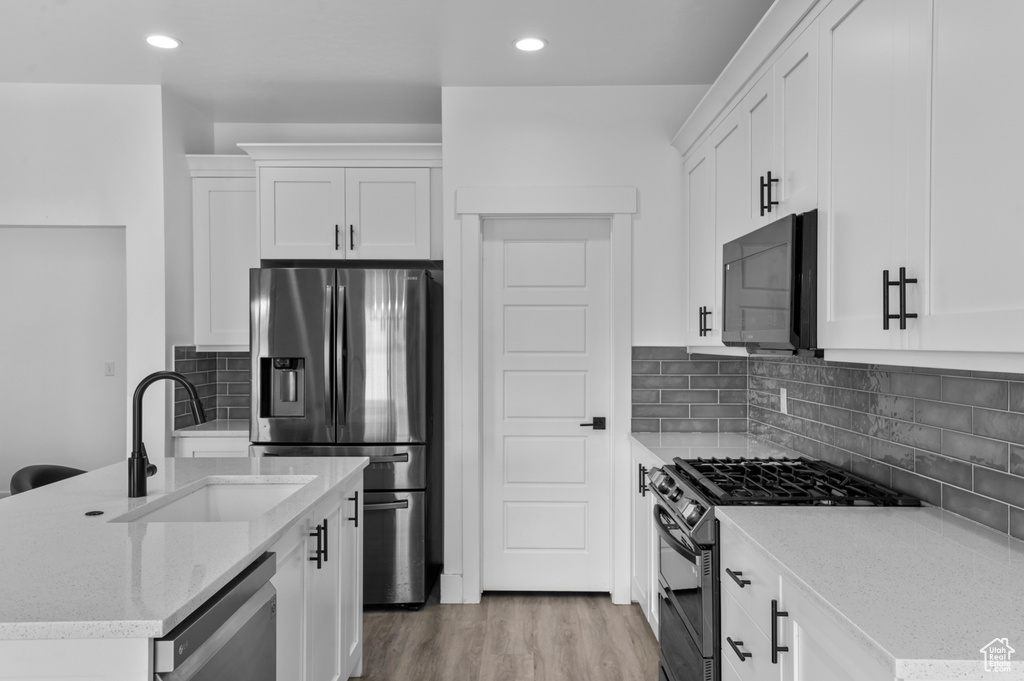 Kitchen featuring stainless steel appliances, a sink, white cabinetry, light stone countertops, and recessed lighting