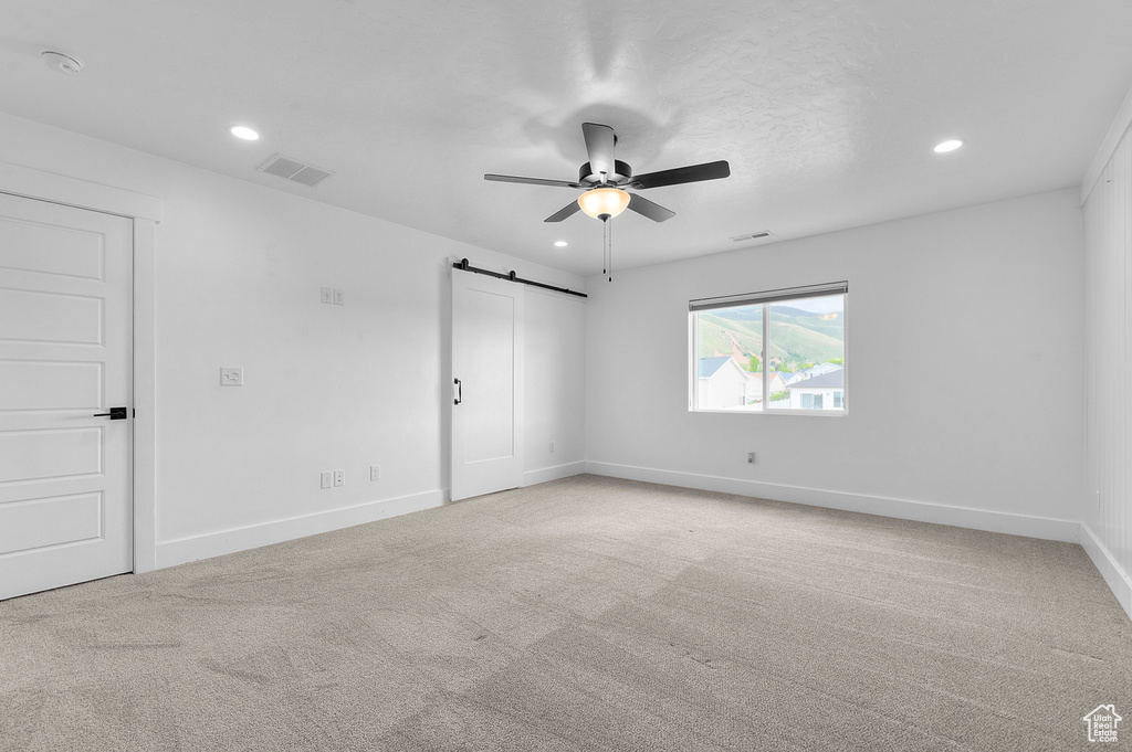 Unfurnished bedroom featuring a barn door, carpet flooring, recessed lighting, baseboards, and a ceiling fan