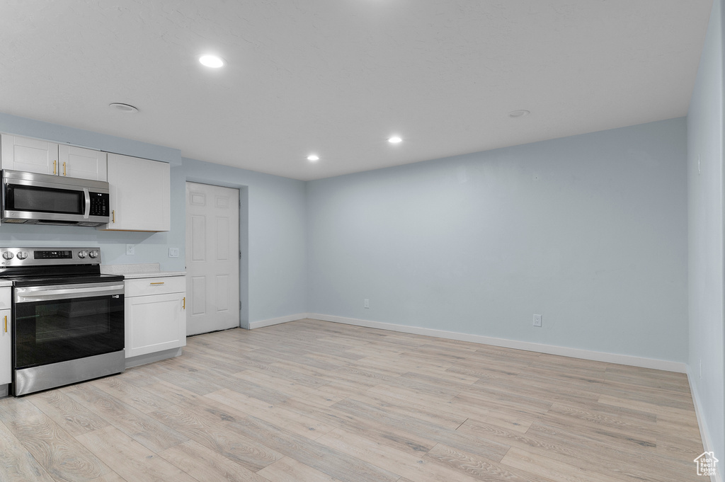 Kitchen with stainless steel appliances, light wood finished floors, white cabinetry, baseboards, and recessed lighting