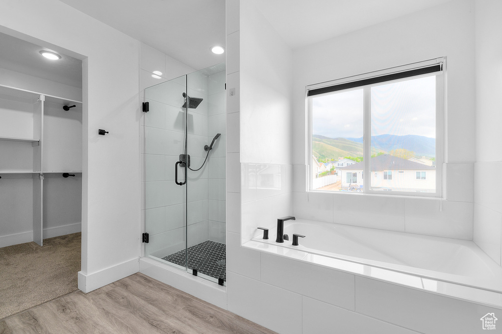 Bathroom featuring a stall shower, wood finished floors, a garden tub, a mountain view, and recessed lighting