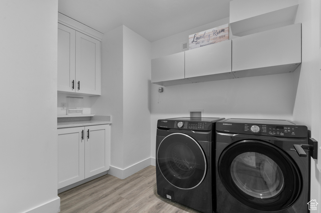 Washroom featuring separate washer and dryer, light wood-style floors, baseboards, and cabinet space